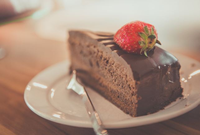 A chocolate cake with a fudge-like topping sits on a small white plate.  According to a study published in a 2019 article at Perishablenews.com, chocolate cake is the most popular searched cake online with over 394,000 search results each month worldwide. 